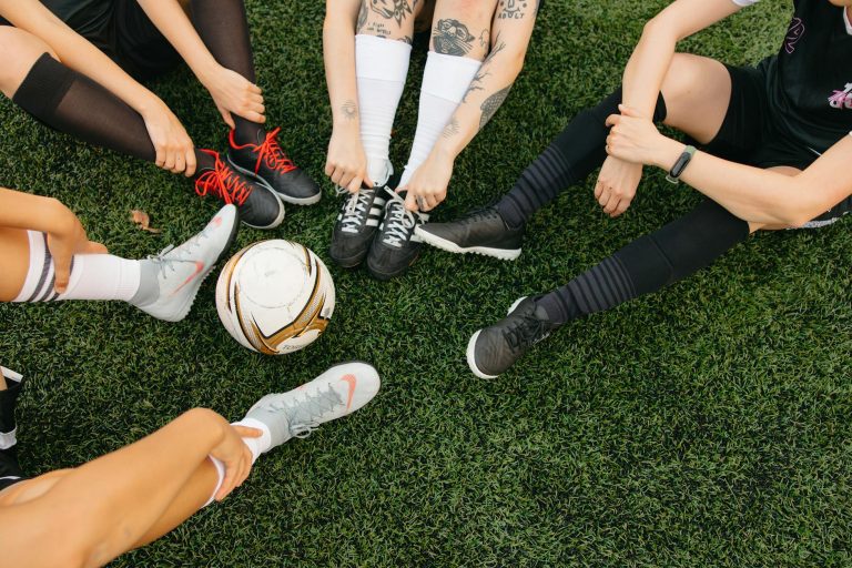 Top view of soccer players tying shoelaces on grassy field before match.