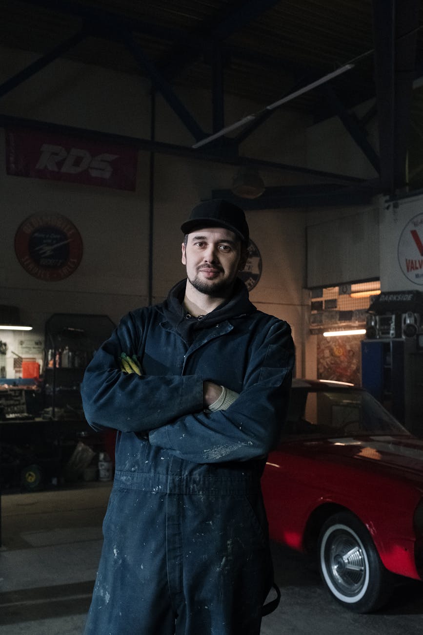 Bearded male mechanic standing confidently in a classic car garage.