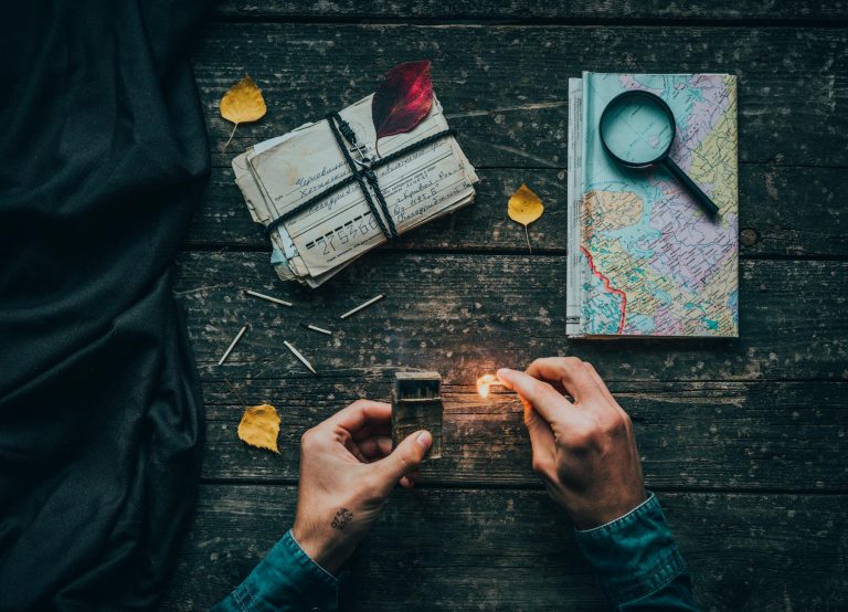 A creative flat lay featuring a map, letters, and a match being ignited on a vintage wooden table.