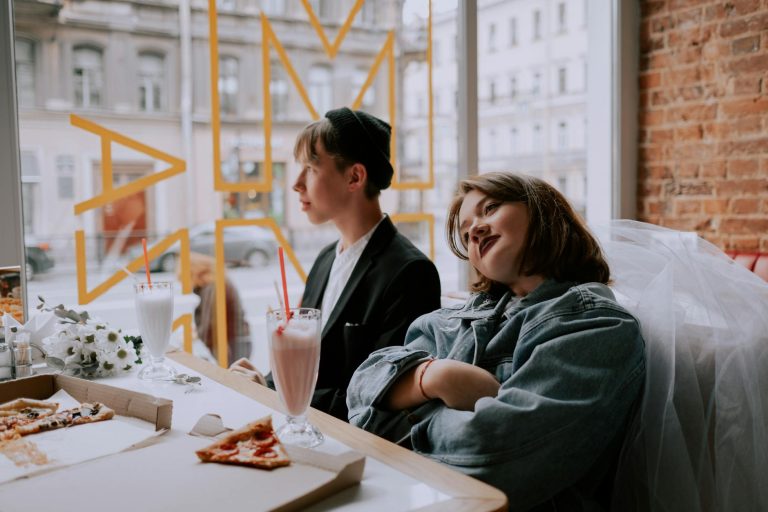 A young couple having milkshakes and pizza at a cozy cafe. Relaxed and joyful atmosphere.