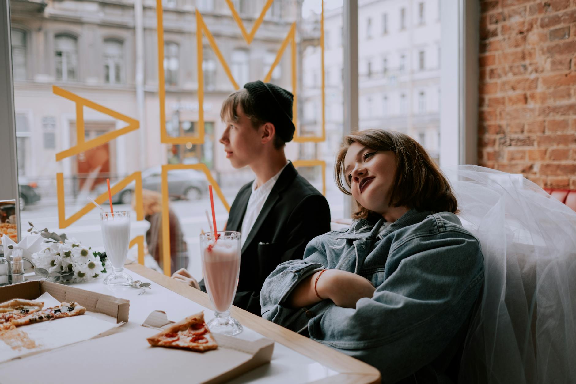 A young couple having milkshakes and pizza at a cozy cafe. Relaxed and joyful atmosphere.