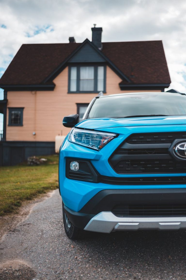 Close-up of a blue SUV parked in front of a rustic country house under a cloudy sky.