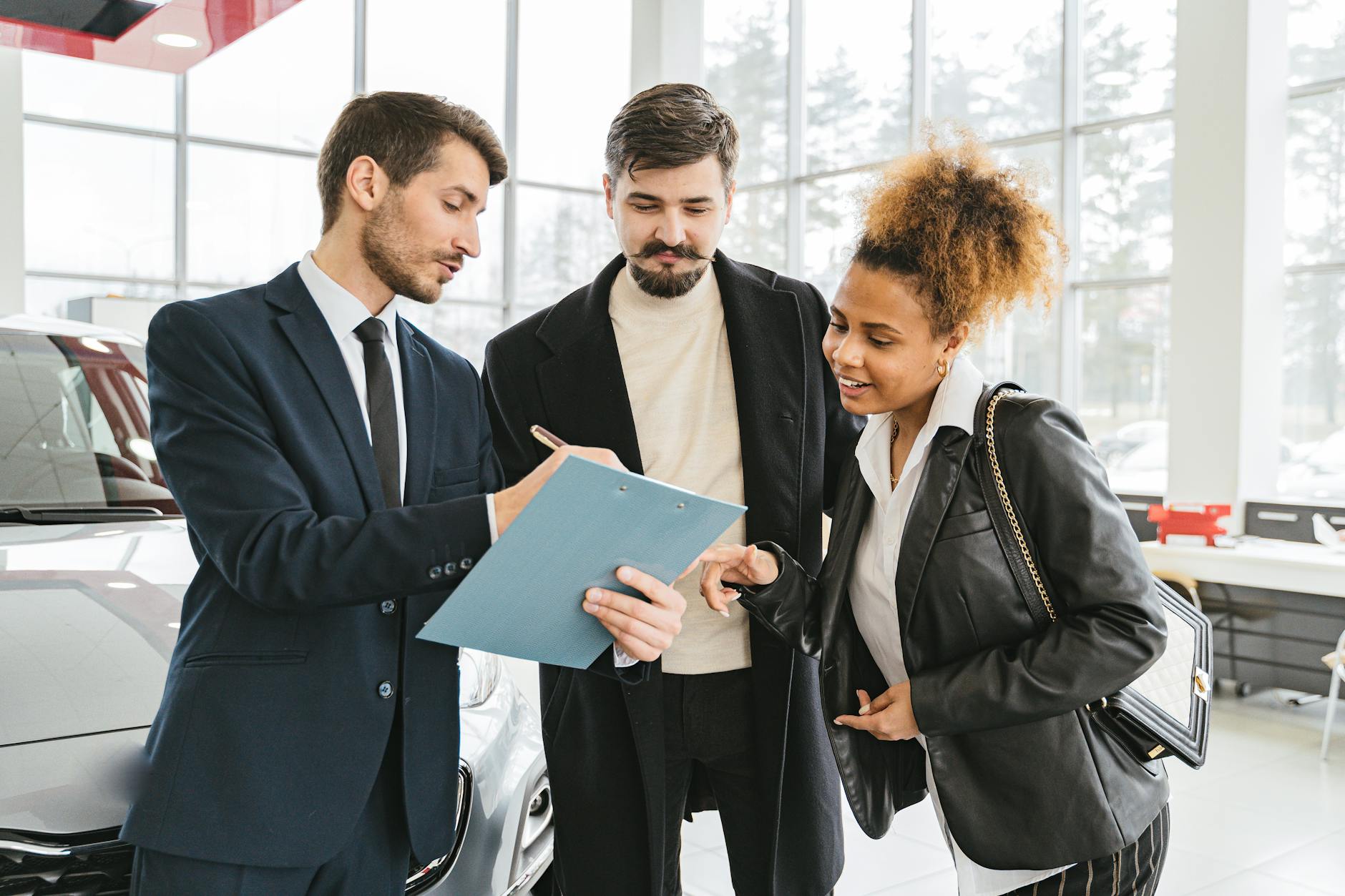 Three business professionals discussing car purchase details inside a modern dealership.