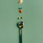 Assorted supplements and a spoon laid out on a green surface, showcasing health concepts.