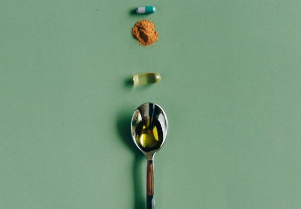Assorted supplements and a spoon laid out on a green surface, showcasing health concepts.