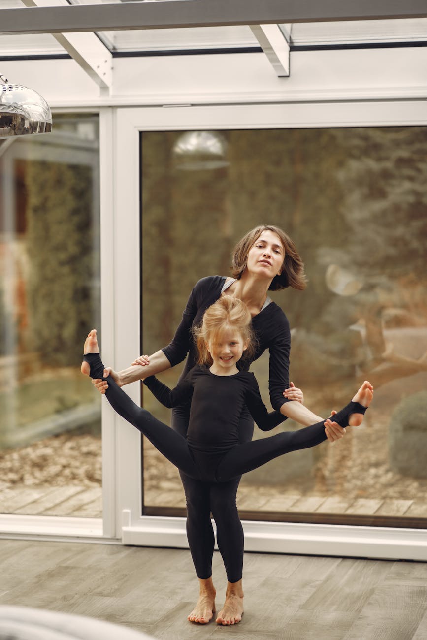 A mother and daughter in black outfits practicing yoga indoors with flexibility and bonding.
