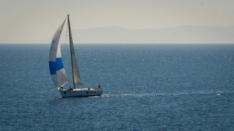 A sailboat glides across a sparkling blue ocean under a clear summer sky, epitomizing leisure and travel.