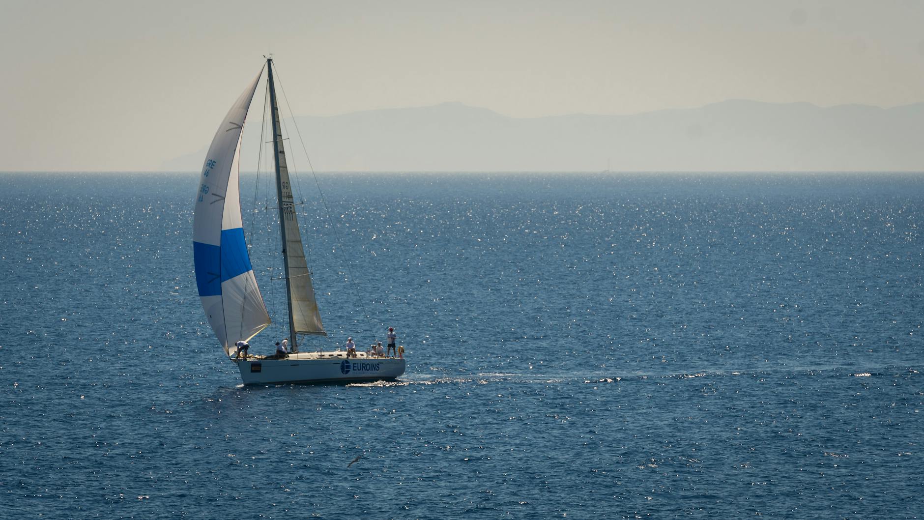 A sailboat glides across a sparkling blue ocean under a clear summer sky, epitomizing leisure and travel.