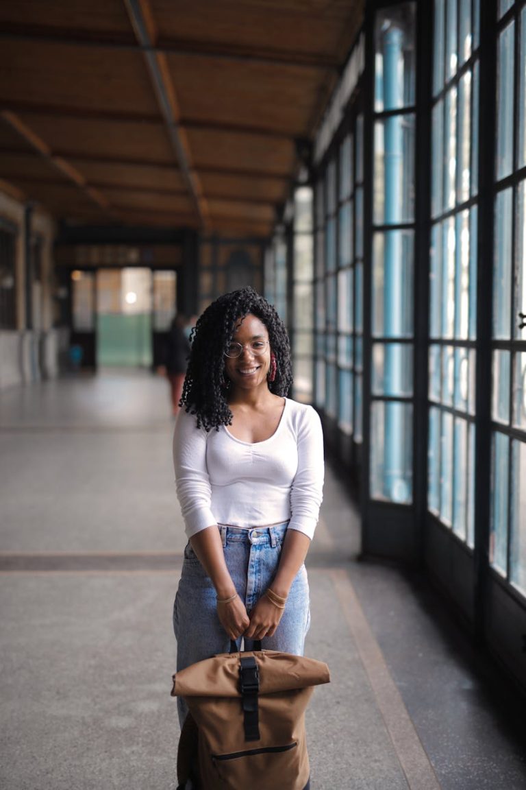 Confident young woman with curly hair standing with a backpack indoors.