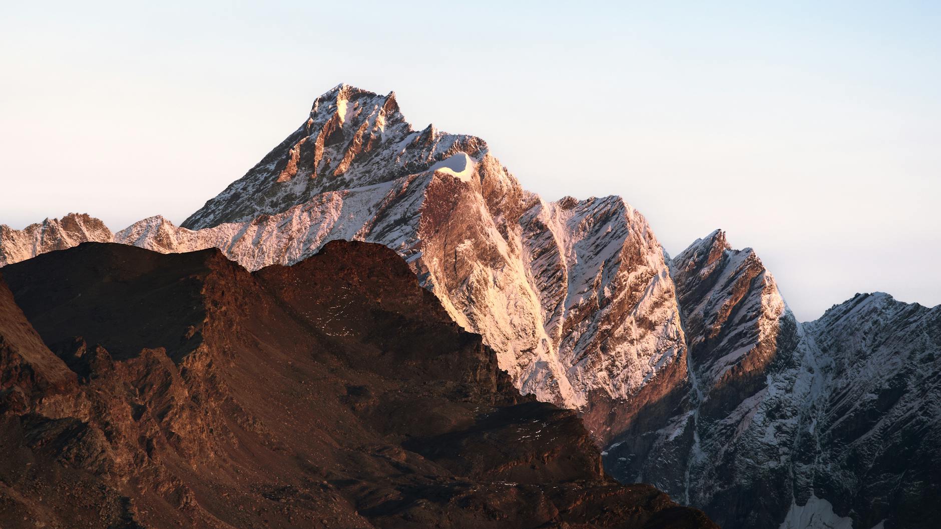 Stunning view of snow-capped alpine peaks at sunrise, showcasing majestic geology and natural beauty.