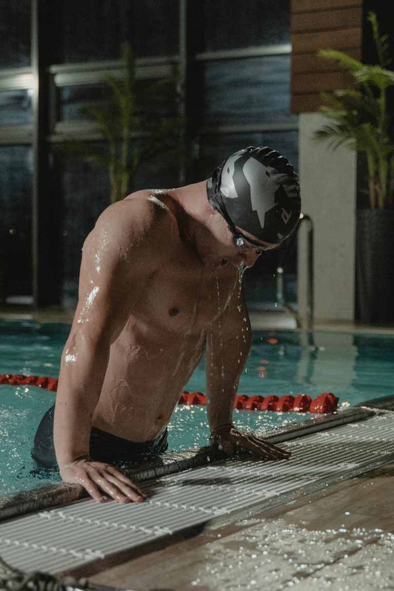 A male athlete in a swim cap exits a swimming pool indoors, demonstrating fitness and determination.